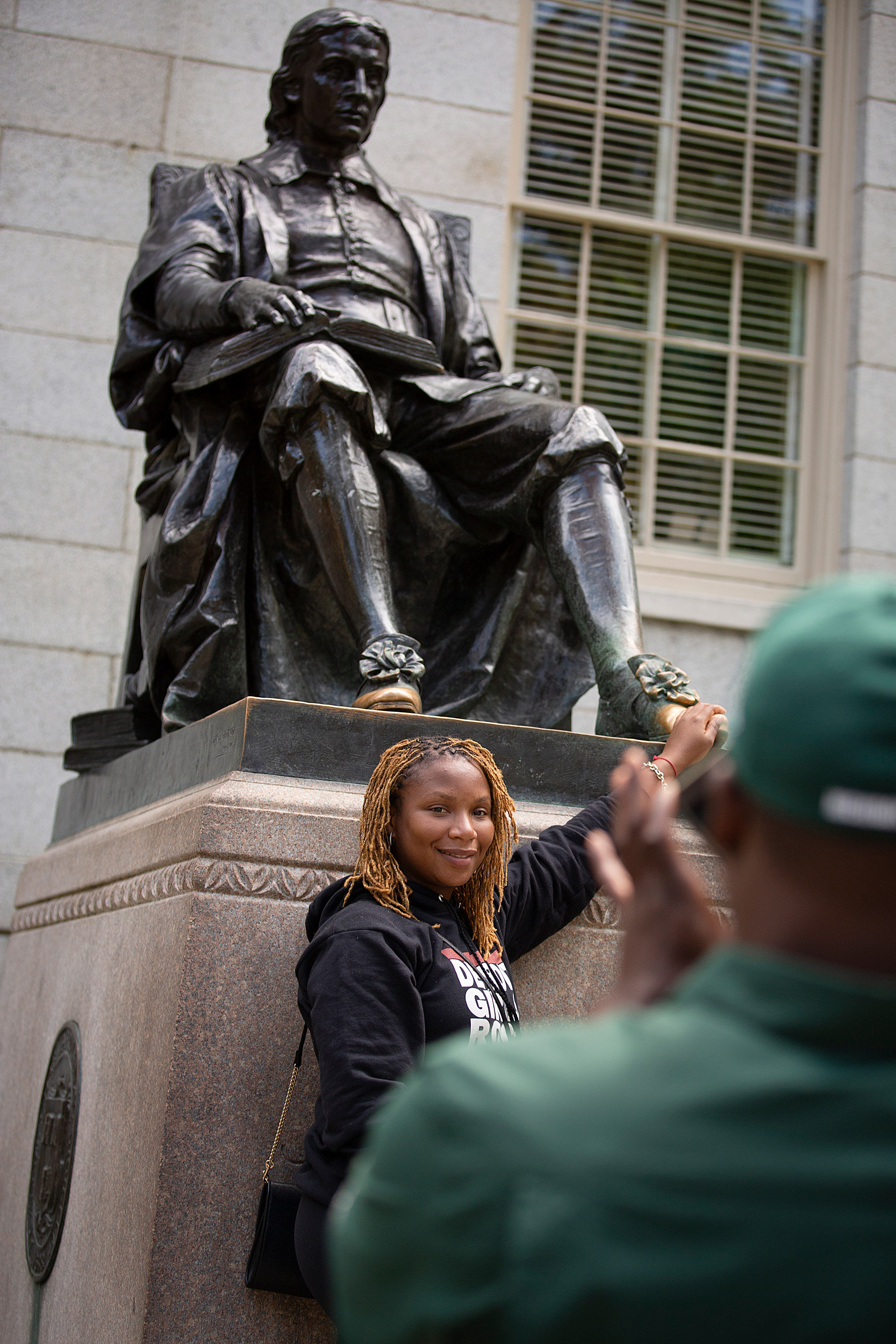 A visitor, Tia Jackson, carefully touches the left foot of the John Harvard sculpture.