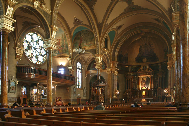 The expansive sanctuary of St. John Cantius Church in Chicago, showcasing soaring columns, round arches, and the golden hues that dominate the interior color palette.