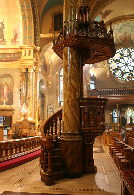 The Baroque Revival pulpit of St. John Cantius Church, featuring ornate wood carvings, a winding staircase, and an elaborate sounding board.