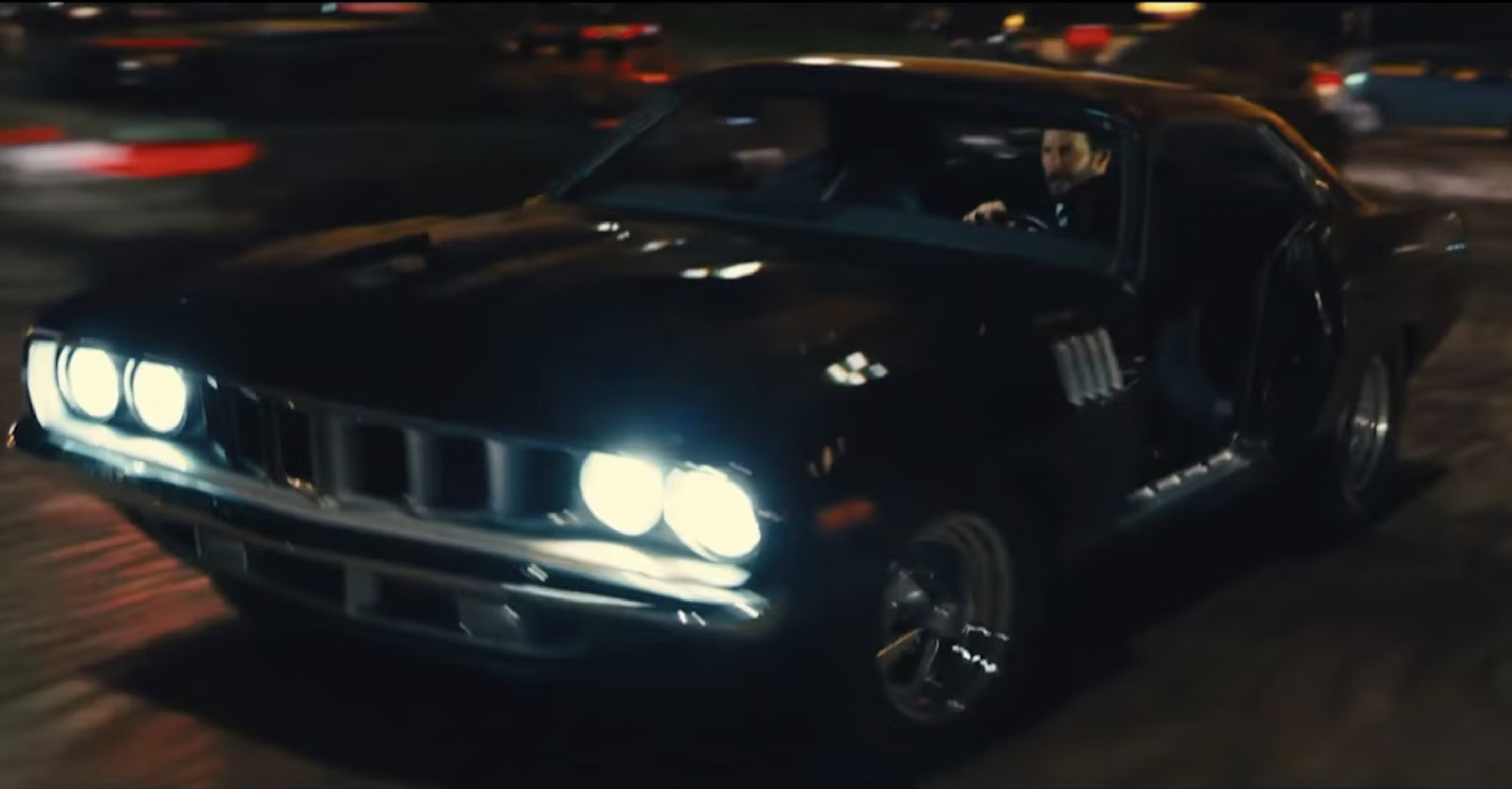 John Wick aggressively driving a black 1971 Plymouth Cuda in a nighttime action sequence from John Wick: Chapter 4.