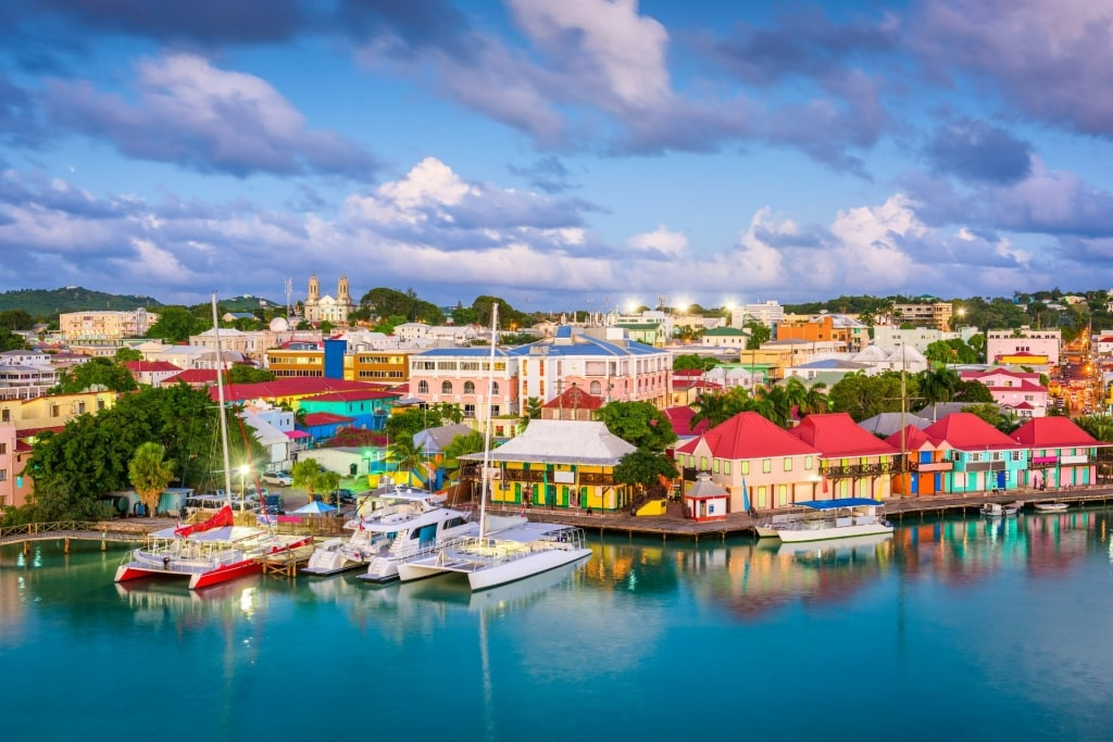 A vibrant waterfront scene at Heritage Quay in Antigua Saint John's, with colorful buildings, shops, and cruise ships docked, offering duty-free shopping and lively atmosphere.