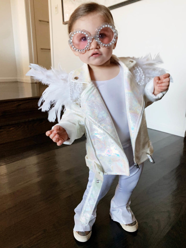 Toddler in a DIY Elton John costume featuring a blue jacket with feather and bead embellishments, flared pants, and star-shaped sunglasses