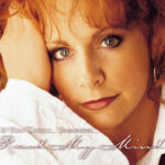 Reba McEntire performing onstage, microphone in hand, at a concert